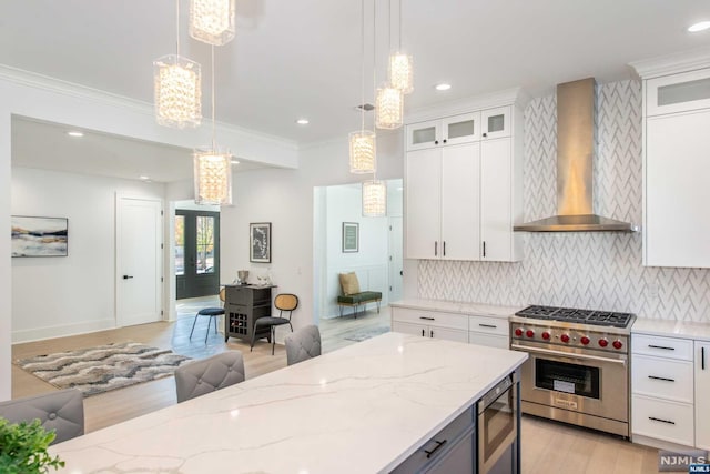 kitchen featuring white cabinetry, stainless steel appliances, decorative light fixtures, and wall chimney range hood