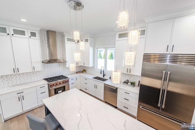 kitchen featuring pendant lighting, white cabinetry, sink, high end appliances, and wall chimney range hood