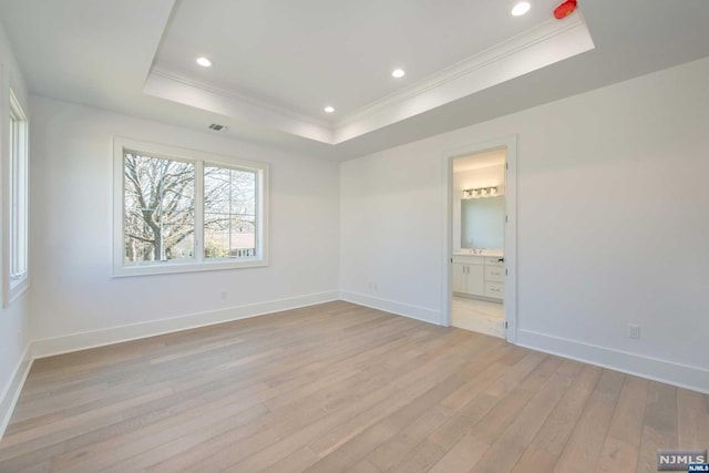 empty room featuring crown molding, a tray ceiling, and light wood-type flooring