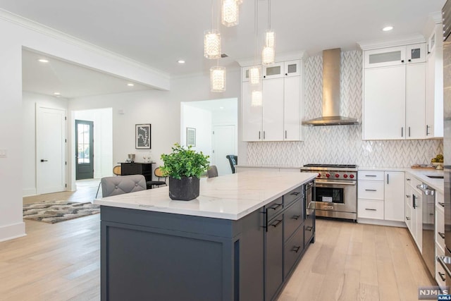 kitchen featuring wall chimney range hood, designer range, hanging light fixtures, and white cabinets