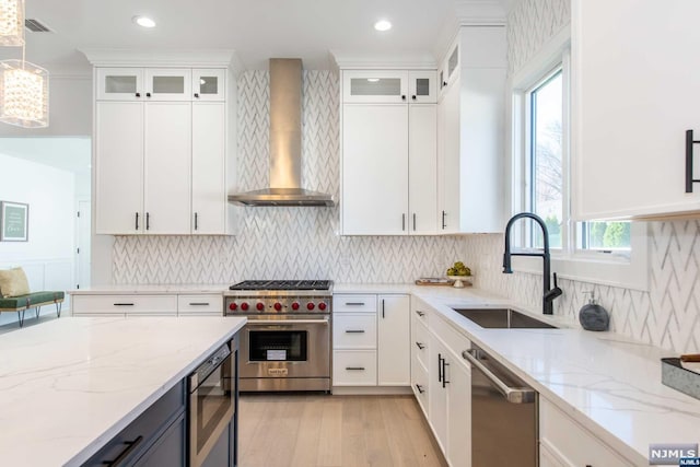 kitchen with sink, decorative light fixtures, wall chimney range hood, stainless steel appliances, and white cabinets