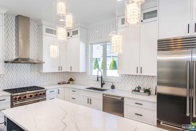 kitchen featuring wall chimney range hood, white cabinets, sink, and high quality appliances