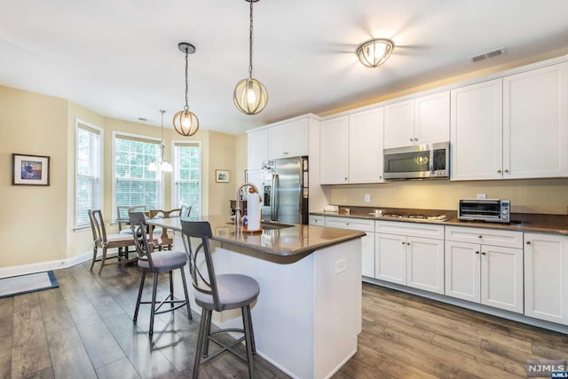 kitchen with dark hardwood / wood-style floors, an island with sink, decorative light fixtures, a breakfast bar, and appliances with stainless steel finishes