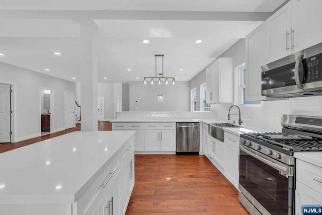 kitchen with appliances with stainless steel finishes, sink, pendant lighting, hardwood / wood-style flooring, and white cabinets