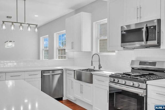 kitchen featuring decorative backsplash, stainless steel appliances, sink, decorative light fixtures, and white cabinetry