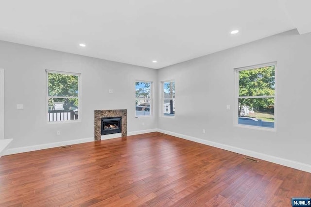 unfurnished living room featuring hardwood / wood-style flooring, a healthy amount of sunlight, and a high end fireplace