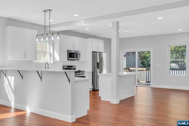 kitchen with a kitchen breakfast bar, white cabinetry, hardwood / wood-style flooring, and appliances with stainless steel finishes