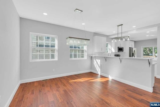 kitchen featuring kitchen peninsula, appliances with stainless steel finishes, white cabinets, hardwood / wood-style floors, and a breakfast bar area