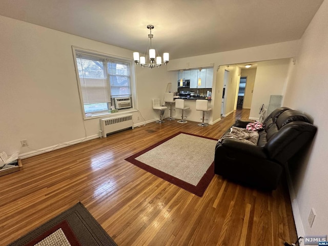 living room with cooling unit, wood-type flooring, radiator, and an inviting chandelier