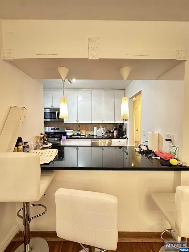 kitchen featuring a breakfast bar, hanging light fixtures, appliances with stainless steel finishes, tasteful backsplash, and white cabinetry