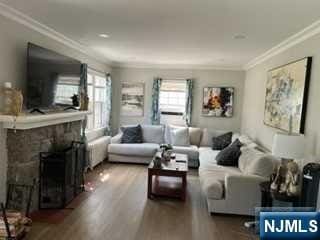 living room featuring hardwood / wood-style flooring, a stone fireplace, and ornamental molding