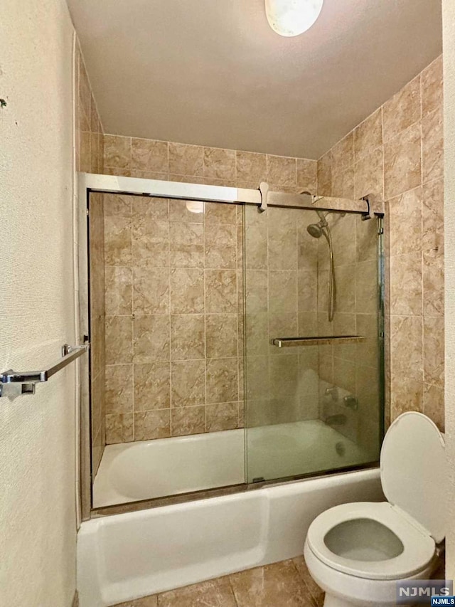 bathroom featuring tile patterned flooring, toilet, and combined bath / shower with glass door