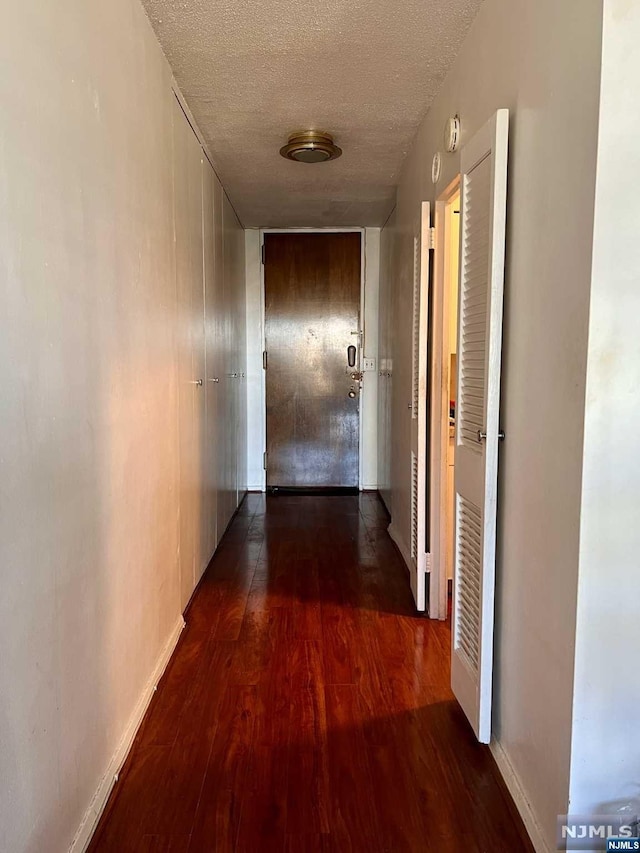 hallway with a textured ceiling and dark hardwood / wood-style flooring