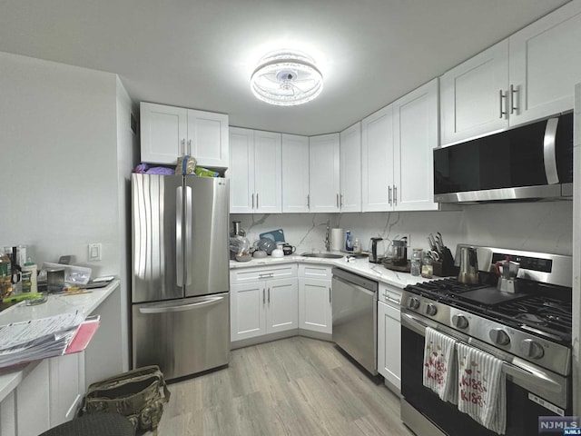 kitchen featuring light stone counters, white cabinets, stainless steel appliances, and light wood-type flooring