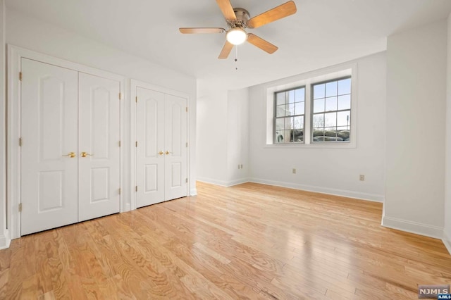 unfurnished bedroom featuring multiple closets, ceiling fan, and light hardwood / wood-style flooring