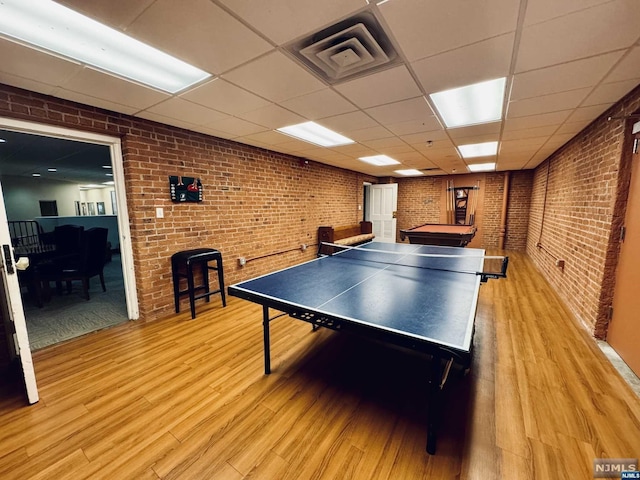 rec room with pool table, a drop ceiling, light wood-type flooring, and brick wall