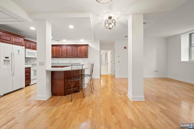 kitchen featuring a breakfast bar, light hardwood / wood-style floors, and white appliances