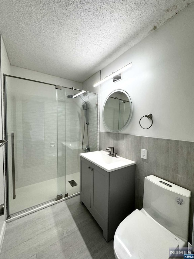 bathroom with toilet, wood-type flooring, a textured ceiling, vanity, and a shower with door