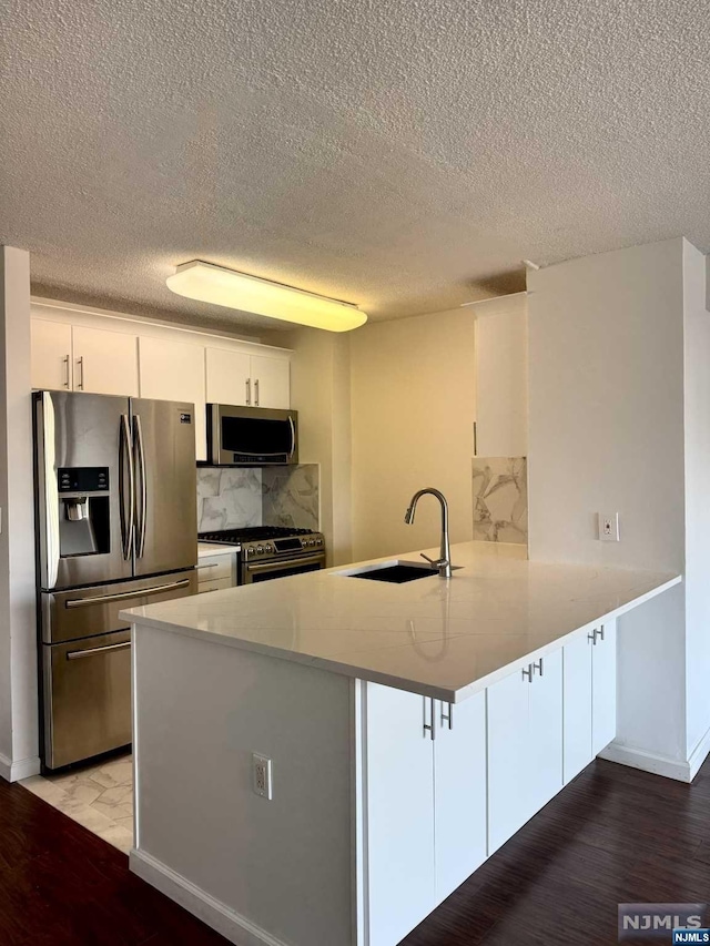 kitchen with sink, stainless steel appliances, tasteful backsplash, kitchen peninsula, and white cabinets