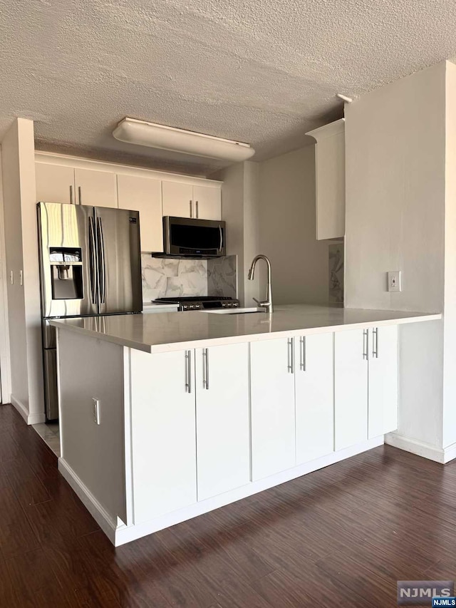 kitchen with dark hardwood / wood-style floors, stainless steel appliances, kitchen peninsula, and white cabinets