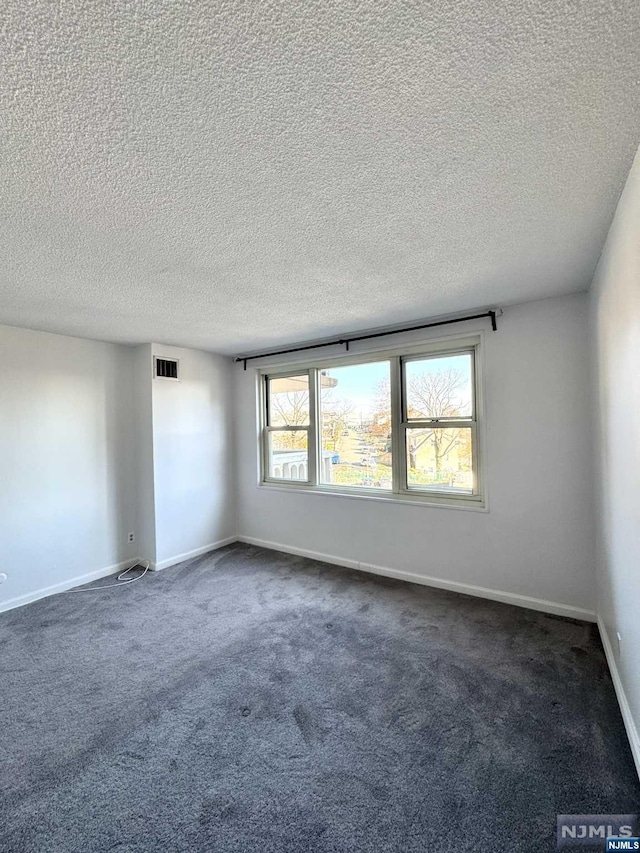 empty room with dark colored carpet and a textured ceiling