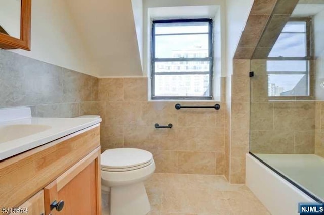 full bathroom featuring vanity, shower / bath combination with glass door, tile patterned flooring, toilet, and tile walls