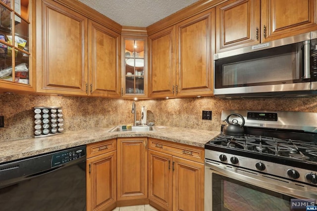 kitchen featuring sink, decorative backsplash, light stone countertops, a textured ceiling, and appliances with stainless steel finishes