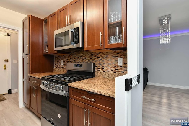 kitchen featuring light hardwood / wood-style flooring, light stone countertops, appliances with stainless steel finishes, tasteful backsplash, and decorative light fixtures