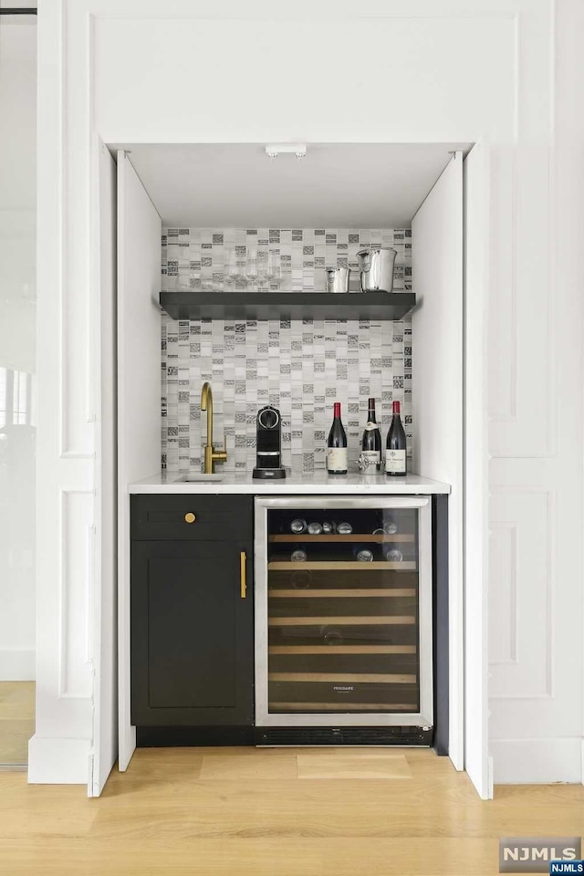 bar with backsplash, wine cooler, light hardwood / wood-style flooring, and sink