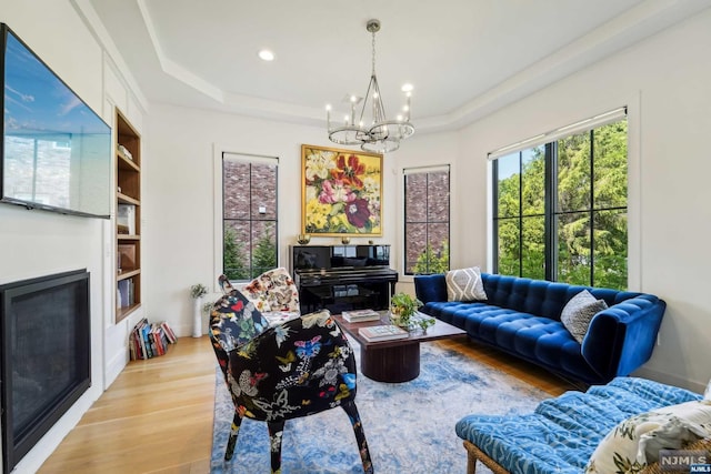 living room featuring a tray ceiling, a notable chandelier, and light wood-type flooring