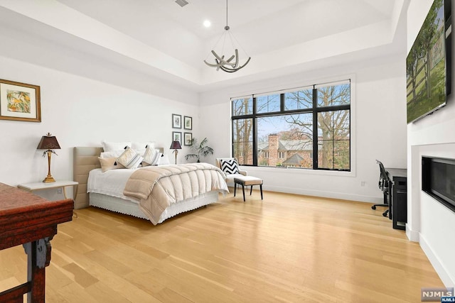 bedroom featuring a raised ceiling, light hardwood / wood-style flooring, and an inviting chandelier