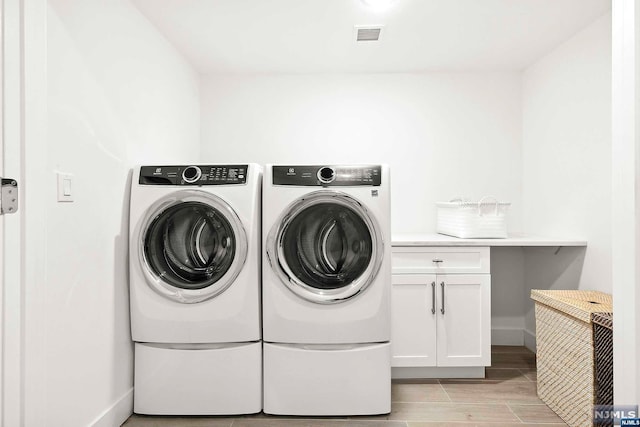 laundry area with cabinets, light wood-type flooring, and washing machine and clothes dryer