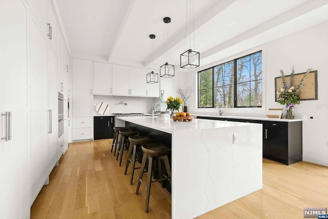 kitchen with a kitchen bar, decorative light fixtures, light hardwood / wood-style flooring, white cabinets, and an island with sink