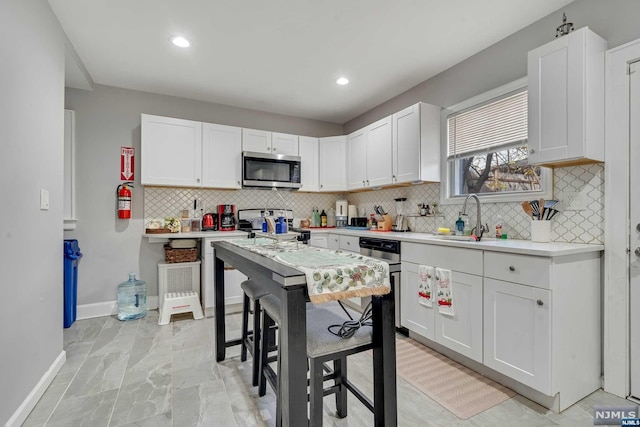 kitchen with a kitchen breakfast bar, stainless steel appliances, white cabinetry, and sink