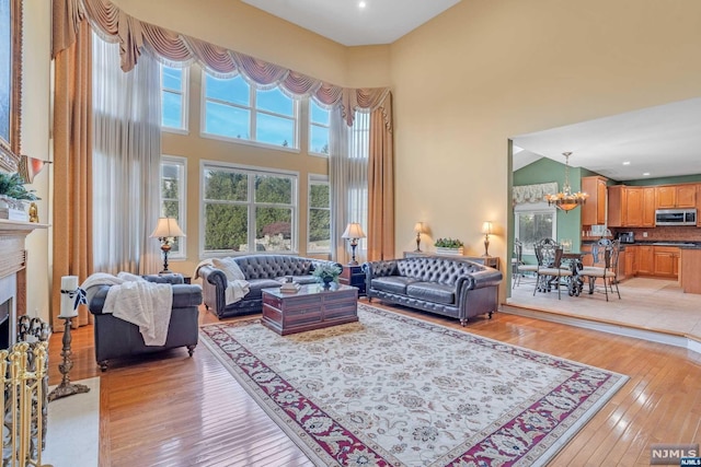 living room featuring an inviting chandelier, a towering ceiling, and light hardwood / wood-style flooring