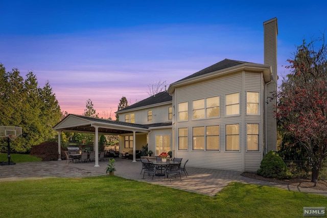 back house at dusk with a lawn and a patio area