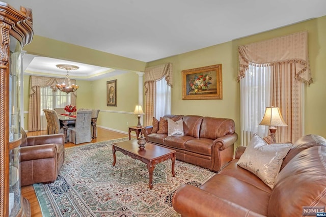 living room with ornate columns, an inviting chandelier, a raised ceiling, crown molding, and hardwood / wood-style floors