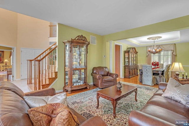 living room with an inviting chandelier, light hardwood / wood-style flooring, decorative columns, a tray ceiling, and ornamental molding