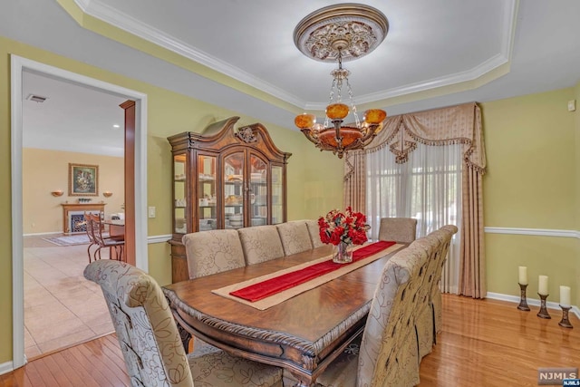 dining room featuring an inviting chandelier, ornamental molding, a tray ceiling, and light hardwood / wood-style flooring