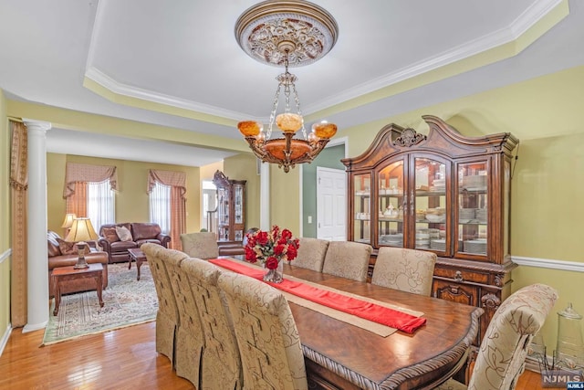 dining room featuring light wood-type flooring, ornate columns, ornamental molding, a tray ceiling, and a notable chandelier