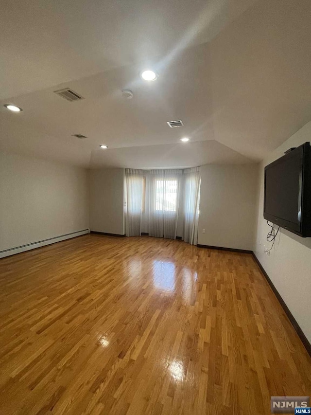 spare room featuring wood-type flooring, a baseboard radiator, and vaulted ceiling