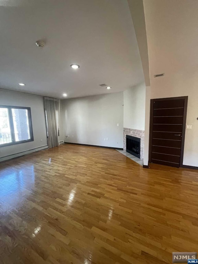 unfurnished living room with hardwood / wood-style floors and a tiled fireplace