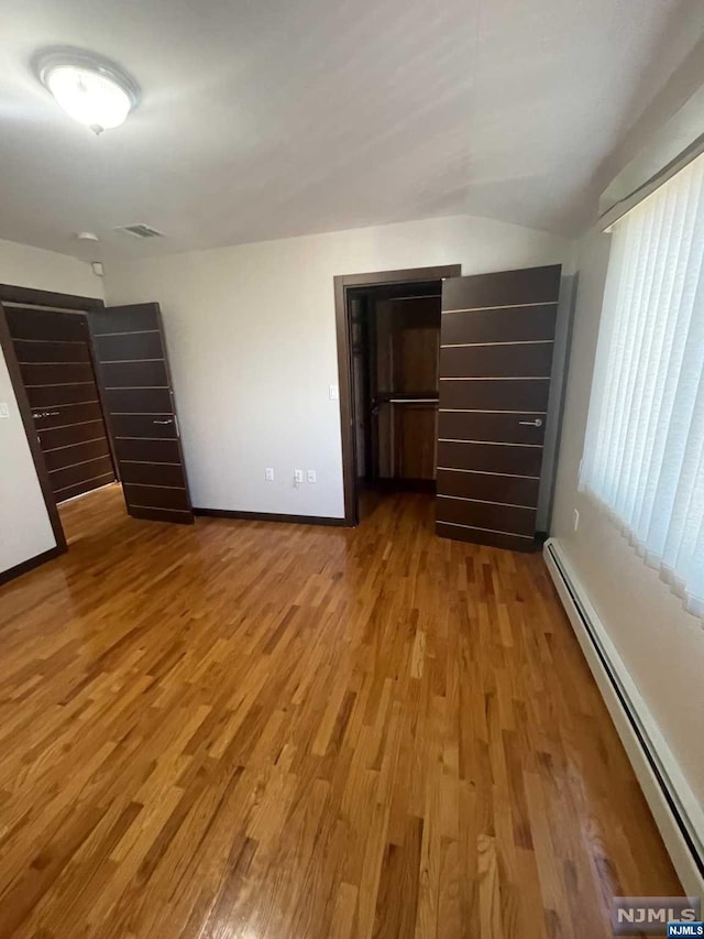 unfurnished bedroom featuring lofted ceiling, wood-type flooring, and a baseboard heating unit