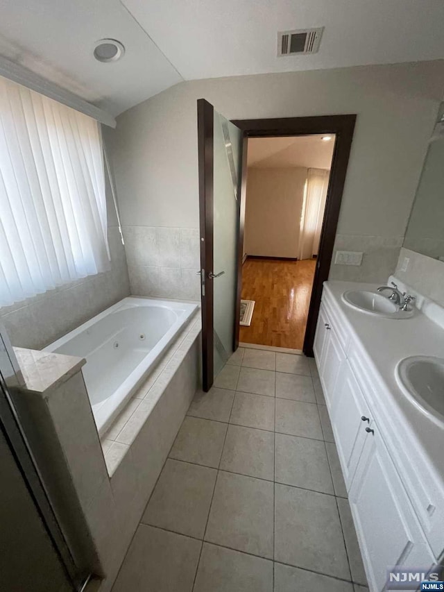 bathroom with tile patterned floors, vanity, lofted ceiling, and tiled tub