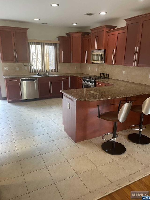 kitchen featuring kitchen peninsula, appliances with stainless steel finishes, dark stone counters, a breakfast bar, and sink