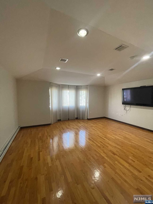 spare room featuring hardwood / wood-style flooring, vaulted ceiling, and a baseboard heating unit