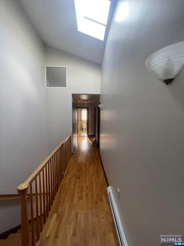 hall featuring hardwood / wood-style flooring, baseboard heating, high vaulted ceiling, and a skylight