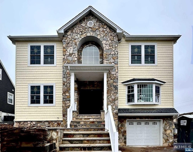 view of front of property featuring an attached garage, stone siding, and central AC unit