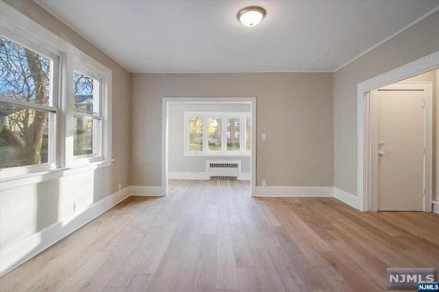 empty room with plenty of natural light, radiator heating unit, and light hardwood / wood-style flooring