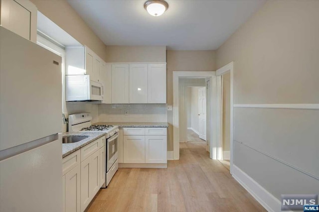 kitchen with light stone countertops, light hardwood / wood-style floors, white appliances, decorative backsplash, and white cabinets